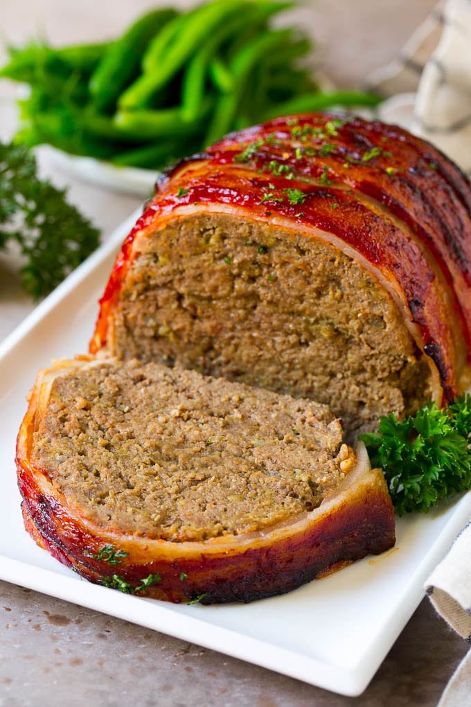 Bacon Wrapped Meatloaf Recipe | Beef Meatloaf #meatloaf #beef #groundbeef #bacon #dinner #jonep A bacon wrapped meatloaf with a slice out of it, on a serving platter.
