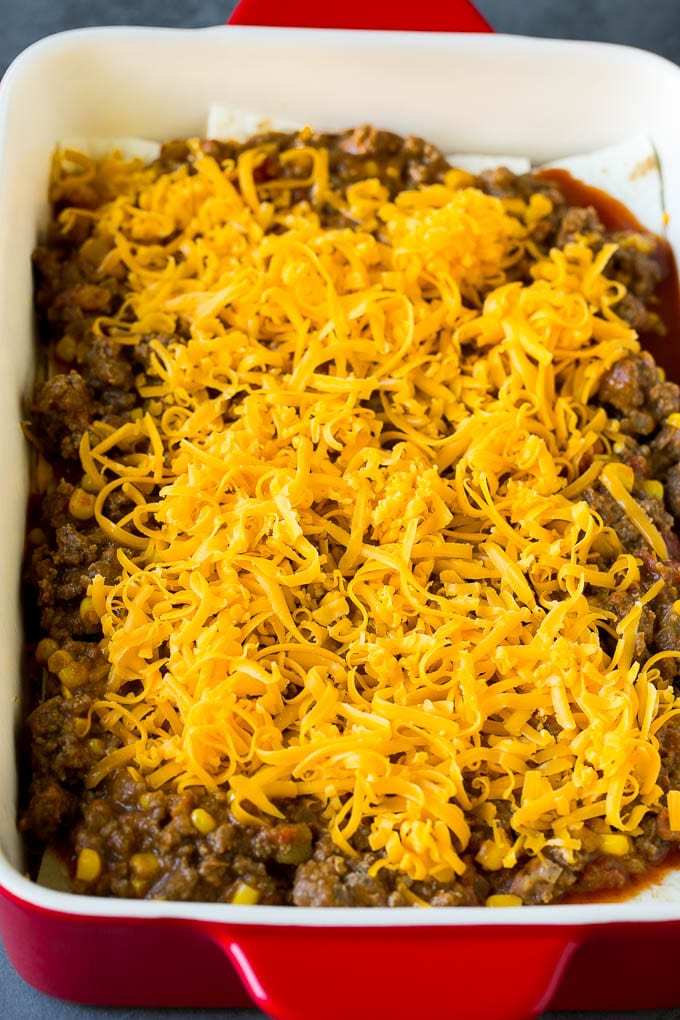 Mexican Lasagna Recipe | Mexican Casserole #mexican #lasagna #groundbeef #beans #dinner #cheese #jonep Layers of tortillas, ground beef and shredded cheese in a baking dish.
