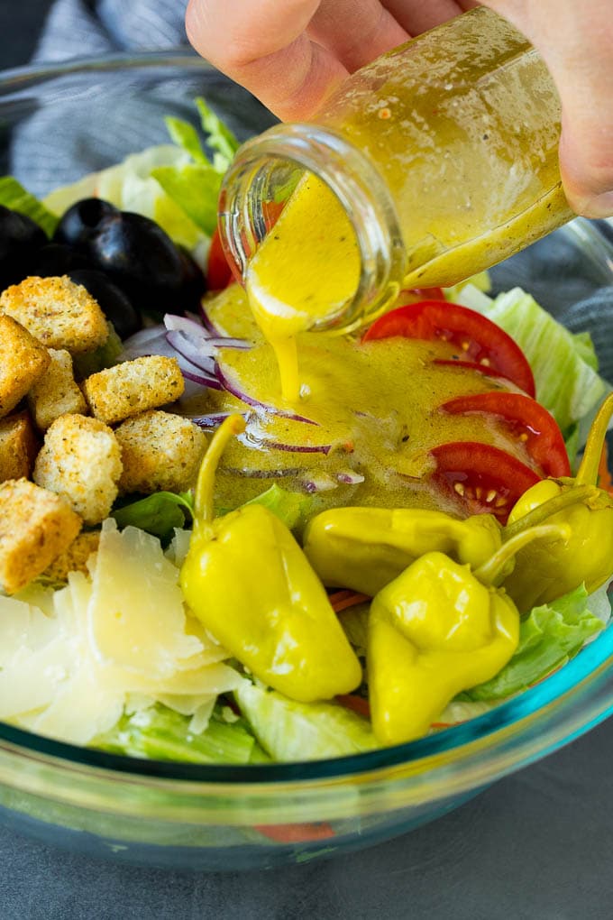Olive Garden Salad Recipe | Italian Salad #salad #lettuce #olives #sidedish #dinner #jonep Dressing being poured over a bowl of salad.