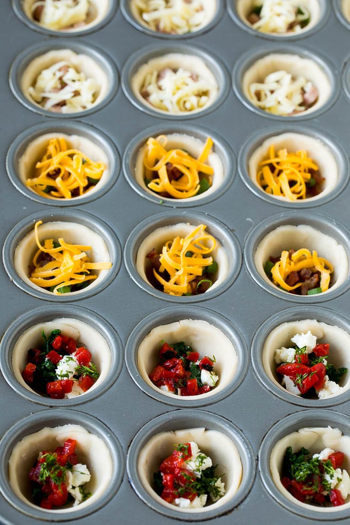 Mini Quiche Recipe #eggs #breakfast #brunch #appetizer #jonep Muffin tins filled with pie crust, vegetables, meat and shredded cheese.