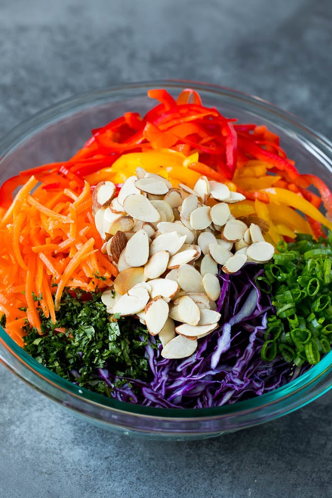 Asian Slaw Recipe #salad #slaw #sidedish #jonep Shredded cabbage, vegetables and almonds in a bowl.