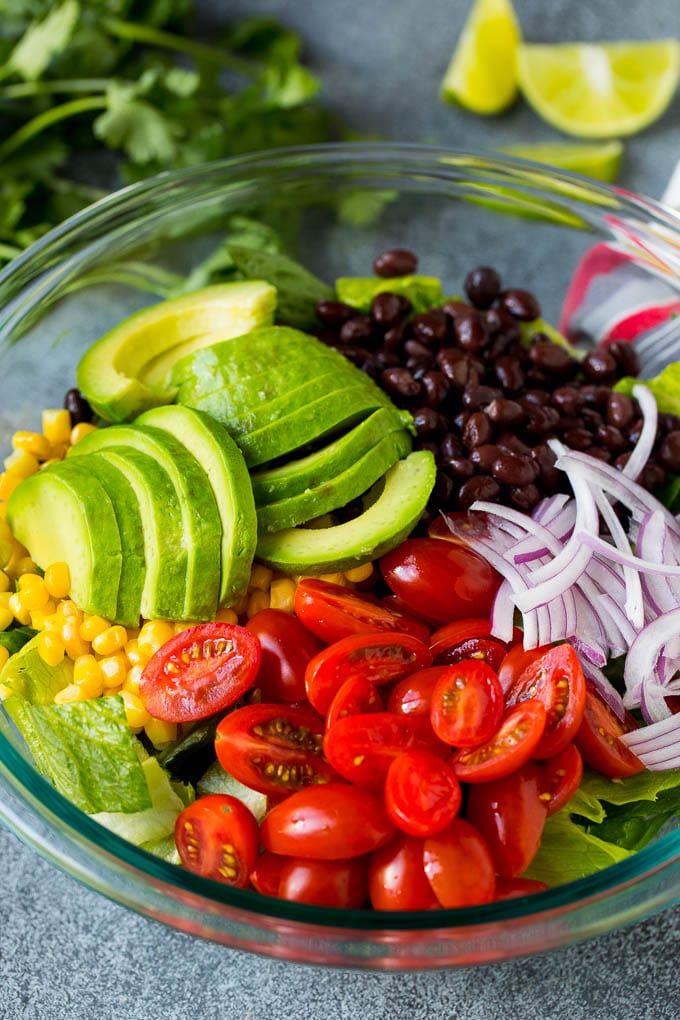 Mexican Salad Recipe #salad #corn #beans #avocado #tomatoes #jonep Lettuce, tomatoes, onion, corn, avocado and black beans in a bowl.