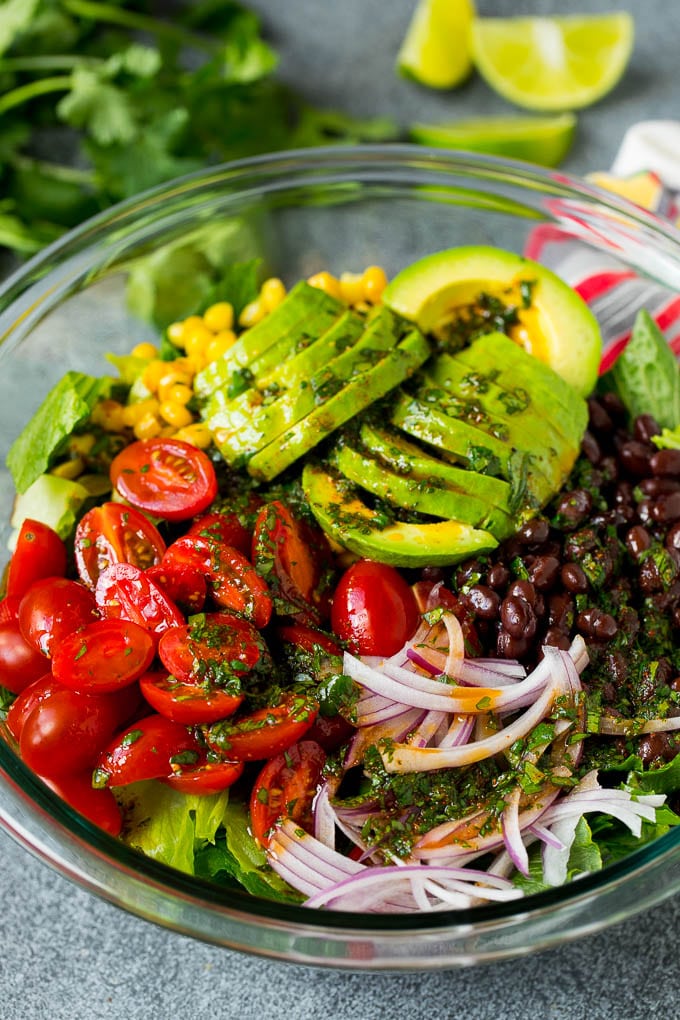 Mexican Salad Recipe #salad #corn #beans #avocado #tomatoes #jonep Dressing poured over a bowl of lettuce, tomatoes, avocado and beans.