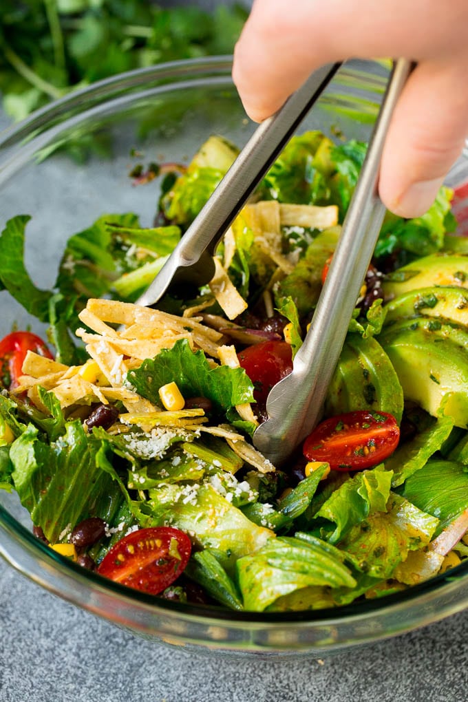Mexican Salad Recipe #salad #corn #beans #avocado #tomatoes #jonep Tongs serving up a portion of Mexican salad.