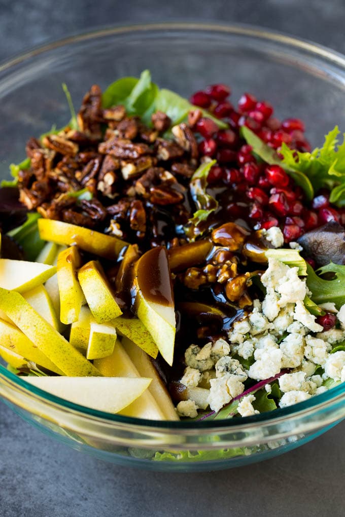 Pear Salad Recipe #salad #pears #fall #winter #dinner #jonep Balsamic dressing poured over a bowl of mixed greens, fruit and pomegranate seeds.
