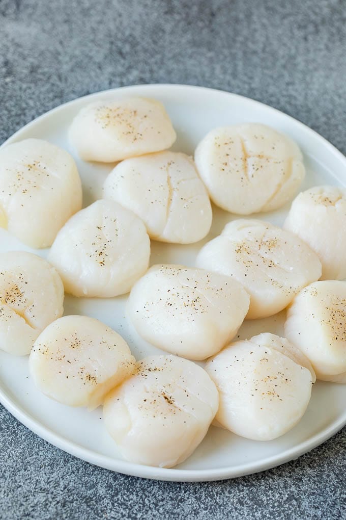 Seared scallops with a garlic and herb butter sauce. An easy and elegant dinner! #seafood #dinner #jonep Raw sea scallops on a plate.