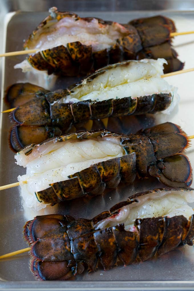 Grilled lobster tail drizzled with garlic butter is an easy and elegant dinner option. #lobster #jonep Raw lobster tails split open with skewers through them.
