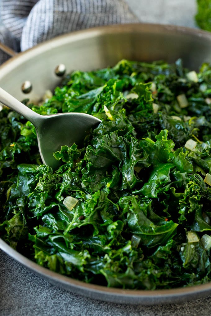 Sauteed kale flavored with olive oil and garlic, a quick and easy side dish! #kale #jonep A pan of sauteed kale with a serving spoon in it.