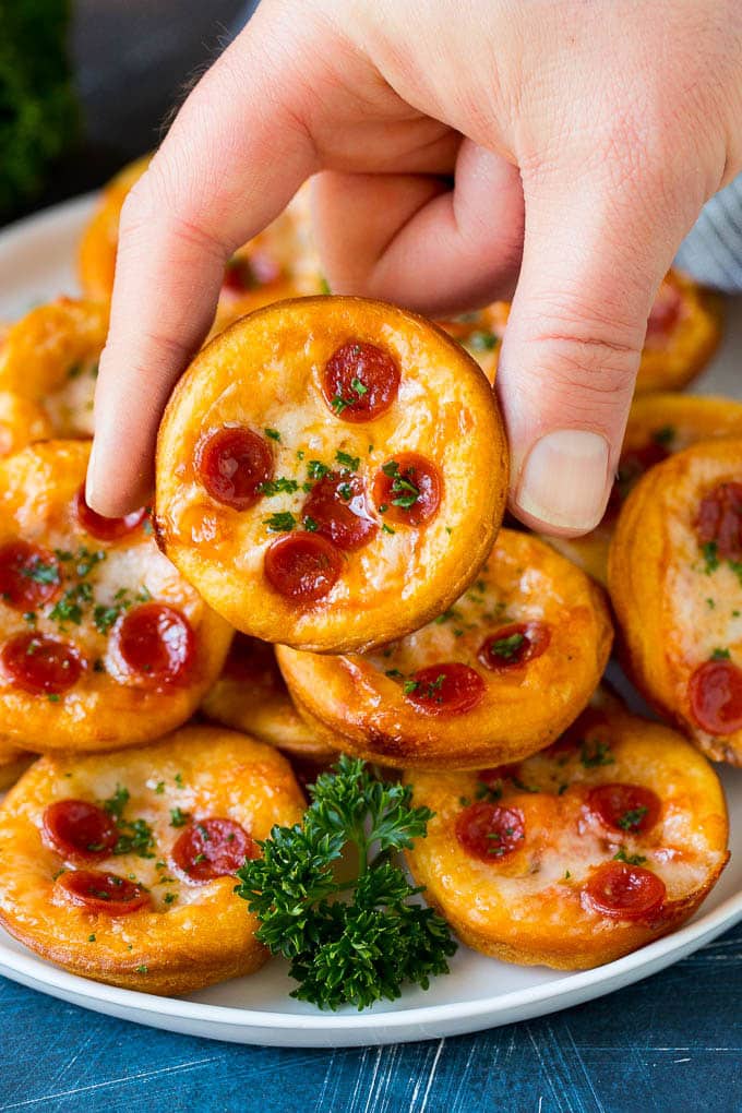Mini pizzas topped with pepperoni are a fun and easy appetizer option. #pizza #jonep #appetizer A platter of mini pizzas with a hand reaching for one.