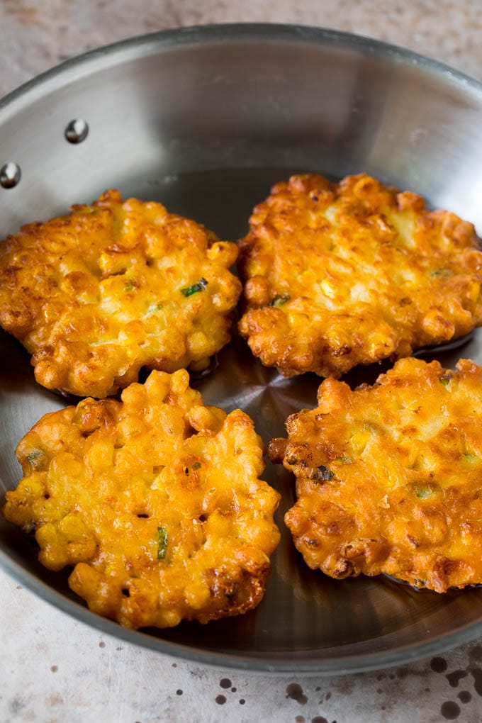 These crispy corn fritters are easy to make and are the perfect appetizer or lighter main course. #corn #jonep Corn cakes in a pan of oil.