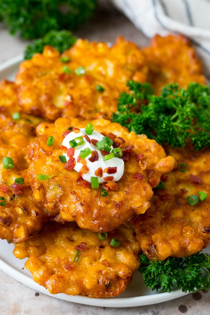 These crispy corn fritters are easy to make and are the perfect appetizer or lighter main course. #corn #jonep A plate of corn fritters garnished with parsley, and topped with sour cream.