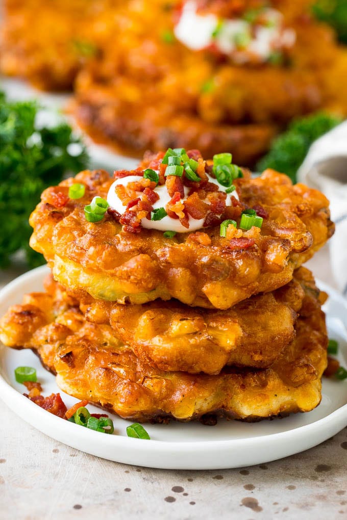 These crispy corn fritters are easy to make and are the perfect appetizer or lighter main course. #corn #jonep A stack of corn fritters topped with bacon, sour cream and green onions.