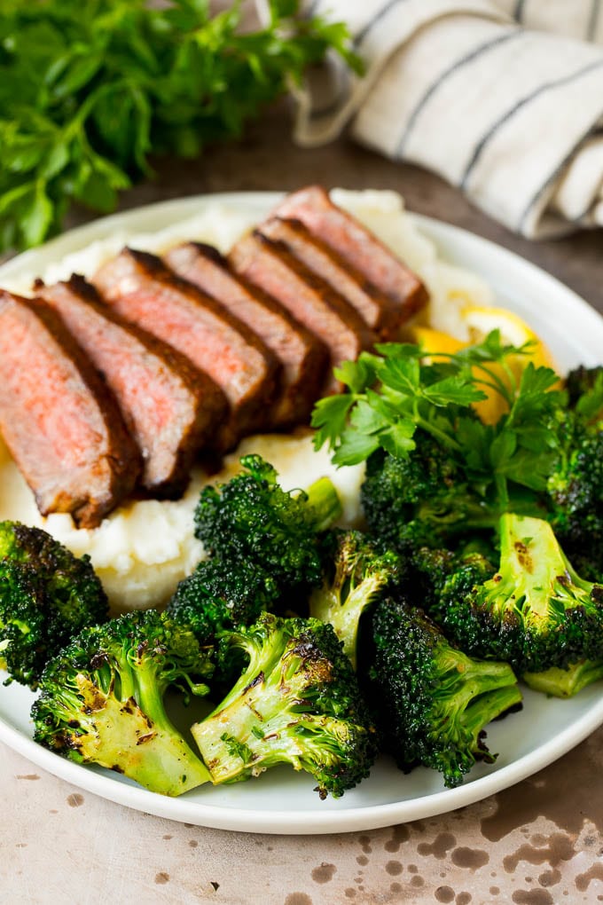 Grilled broccoli is packed with flavor and is a colorful and healthy side dish! #broccoli #jonep Grilled broccoli on a plate with steak and mashed potatoes.