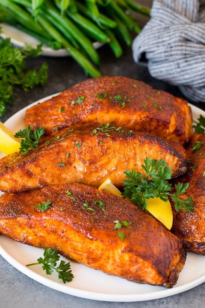 This air fryer salmon is fresh fish fillets topped with a homemade spice rub, then cooked to golden brown perfection. A plate of air fryer salmon fillets garnished with lemon and herbs.