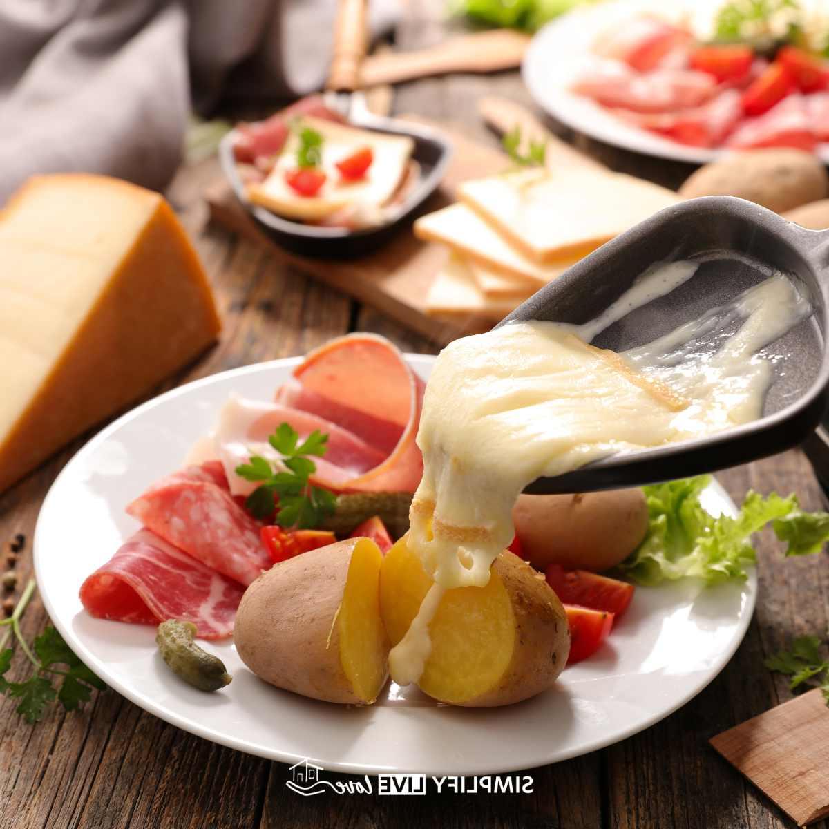 Gesmelte raclette-kaas in 'n braaipan oor gekookte aartappels met ander vleise en groente op 'n bord en in die agtergrond vir 'n partytjie