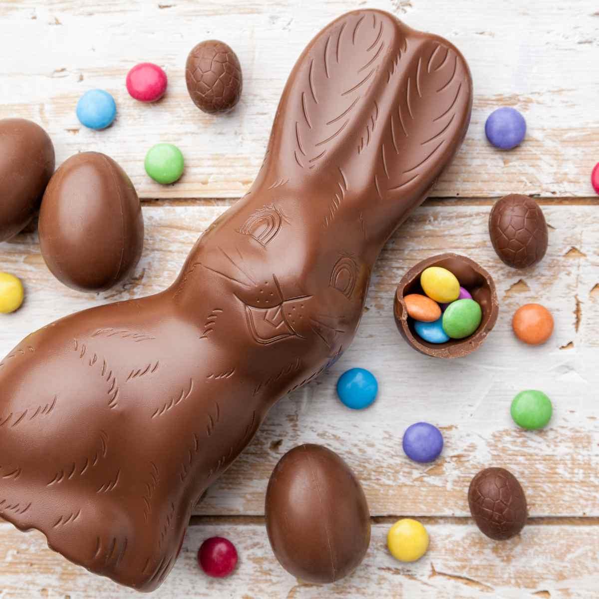 Duik in die Lente: 9 Gesonde Paasmandjie-Idees 2 Melksjokolade Paashaas met kleiner sjokolade Paaseiers en gekleurde lekkers op toonbank