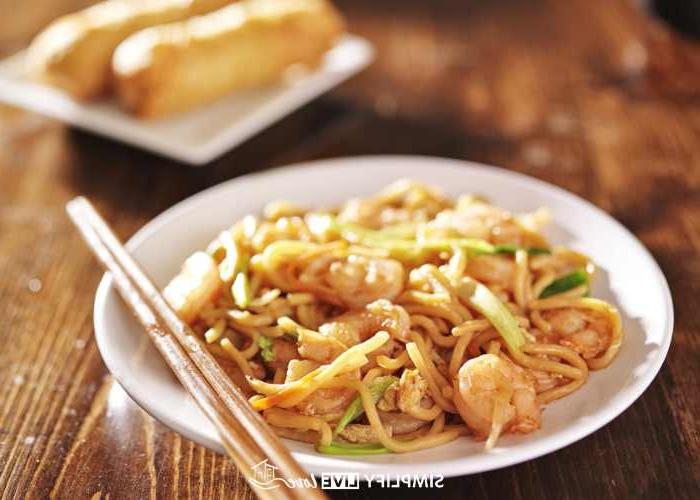 Maklike Resep vir Krokante Tuise Eierrolletjies met Boontjiespruite 4 garnale lo mein met eetstokkies op 'n wit bord en eierrolletjies as bygereg