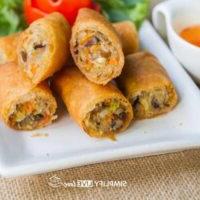 Maklike Resep vir Krokante Tuise Eierrolletjies met Boontjiespruite 5 eierrolletjies in die helfte gesny en op wit bord gestapel met bed van blaarslaai