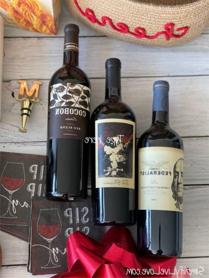 6 Συμβουλές για Εύκολα και Όμορφα Οινικά Καλάθια Δώρων 4 Τρία μπουκάλια κρασί με χρυσό πώμα κρασιού και χαρτοπετσέτες κοκτέιλ στο φόντο για καλάθια κρασιού και τυριού
