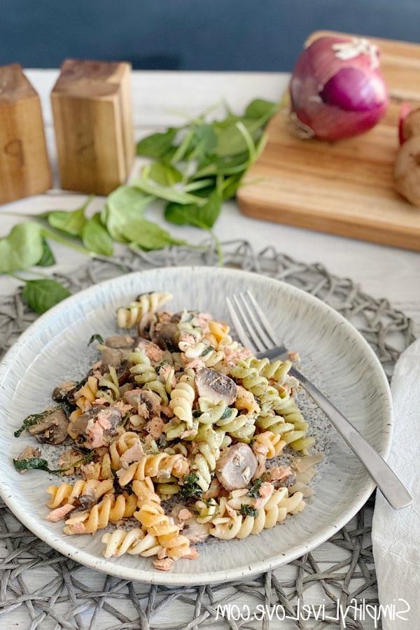 Kaasagtige Salm Pasta met Spinasie en Sampioene 6 delicious salmon pasta on a white white plate with onions and spinach leaves in background