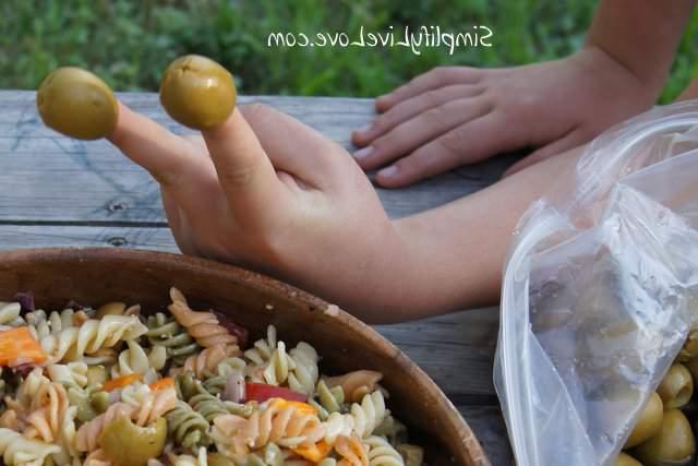 SONY DSC kid holding green olives on their fingers next to a bowl of asiago pasta salad
