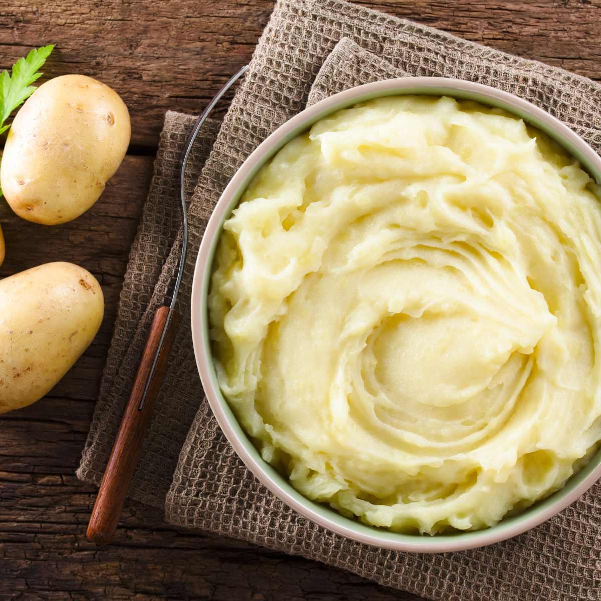 Τέλειος Instant Pot Πουρές Πατάτας (+ Συμβουλές Κατάψυξης & Αναθέρμανσης) 2 Κρεμώδης πουρές πατάτας σε μπολ, με ωμές πατάτες δίπλα σε τραπέζι