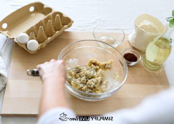 Συνταγές για Γρήγορα και Εύκολα Σπιτικά Μείγματα Ψησίματος που θα Λατρέψετε 3 Γυναίκα ανακατεύει muffins σε γυάλινο μπολ με χαρτοκιβώτιο αυγών και βάζο λαδιού στον πάγκο