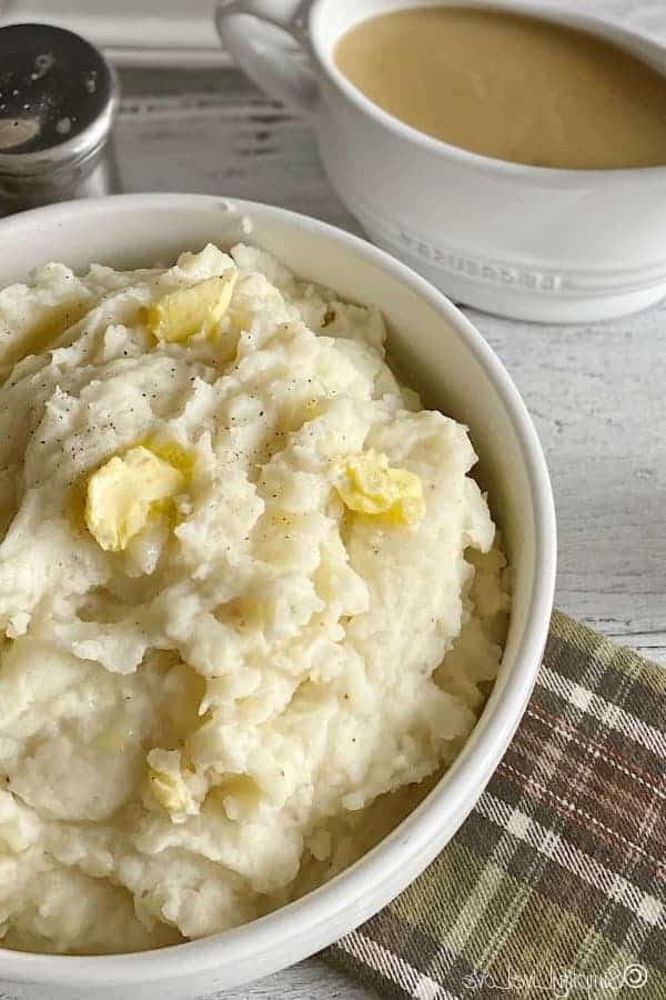 Τέλειος Instant Pot Πουρές Πατάτας (+ Συμβουλές Κατάψυξης & Αναθέρμανσης) 6 Κομμάτια βουτύρου λιωμένα σε μπολ με πουρέ πατάτας με δοχείο σάλτσας στο βάθος