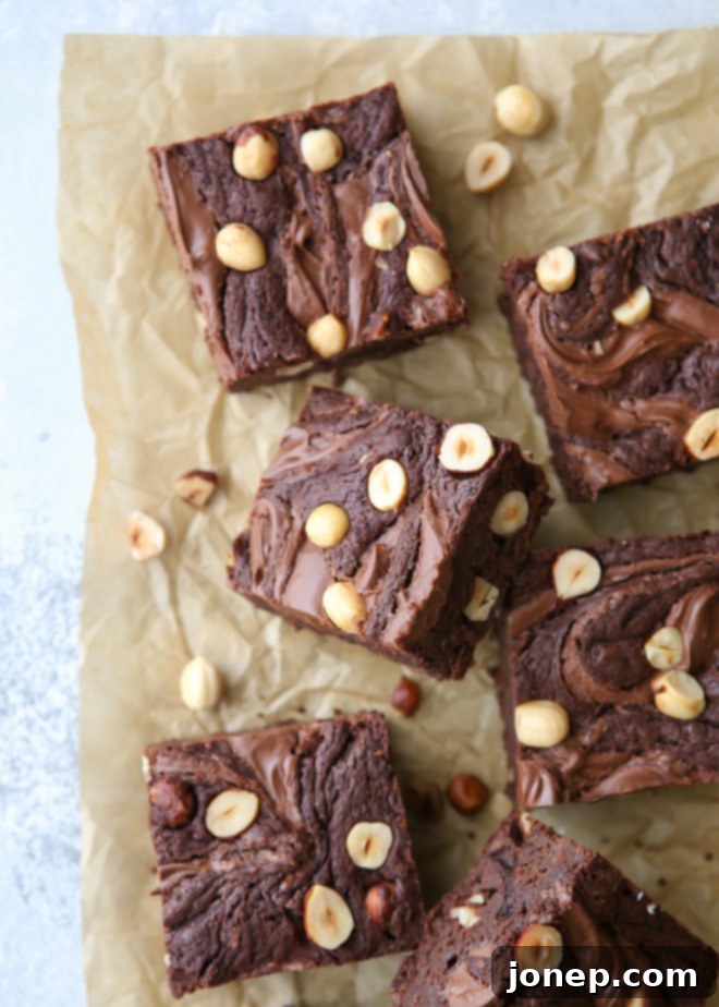A slice of Nutella brownie with hazelnuts on a plate, showing its fudgy interior and distinct swirl