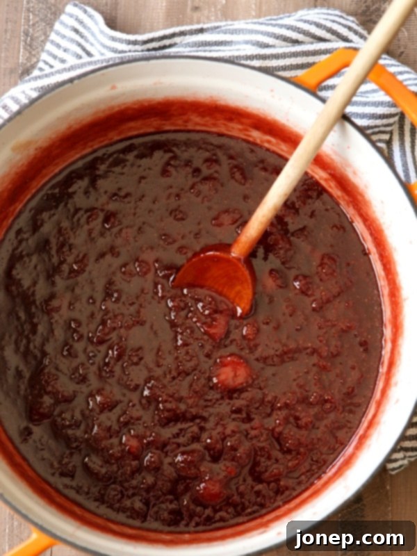 Strawberry jam simmering in a large pot, showing the process of reduction and thickening.