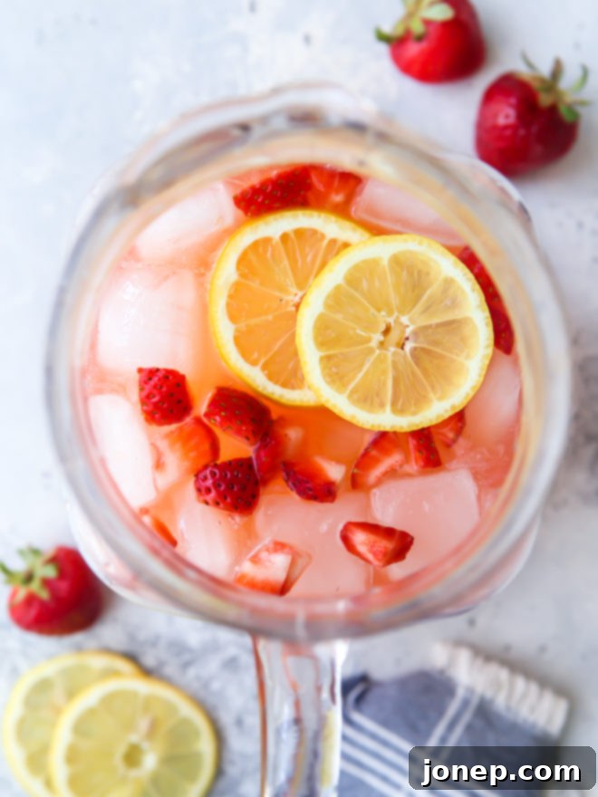 Effortless Strawberry Lemonade 2 Pitcher of homemade strawberry lemonade with sliced lemons and fresh strawberries
