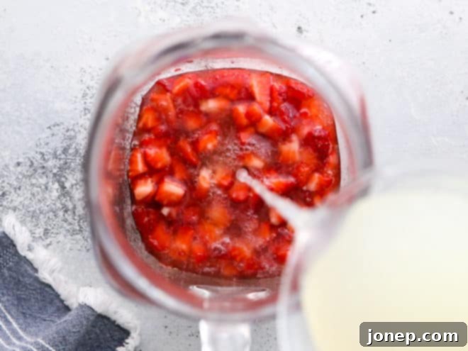Effortless Strawberry Lemonade 5 Pouring store-bought lemonade into a pitcher with macerated strawberries and ice