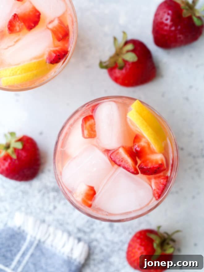 Effortless Strawberry Lemonade 6 Close-up of a glass of strawberry lemonade garnished with a lemon slice and a fresh strawberry, on a rustic surface