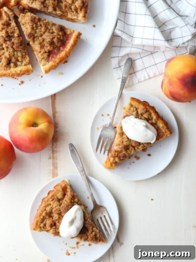 A slice of baked peach crumb tart with a golden streusel topping and juicy peach filling, served on a white plate.