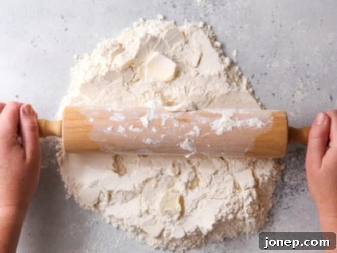 Rolling cold butter into dry ingredients on a clean surface with a rolling pin.