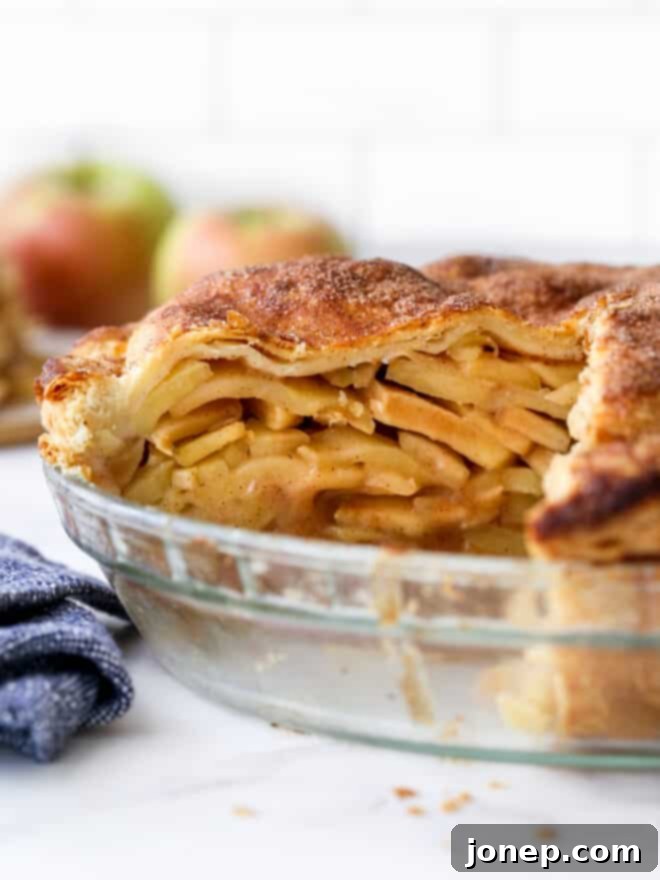 A close-up of a perfectly cut slice of mile-high apple pie still in the pan, showcasing the layers of apples.