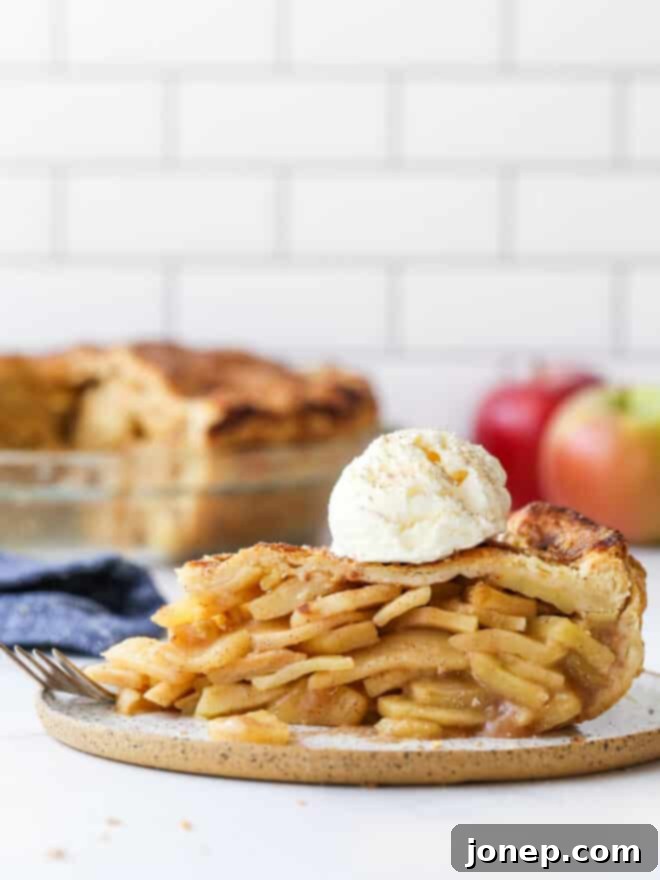 A beautiful slice of mile-high apple pie on a plate, with the whole pie blurred in the background.