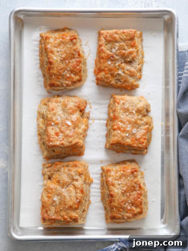 A hand reaching for a warm, freshly baked whole wheat cheddar biscuit on a wooden board