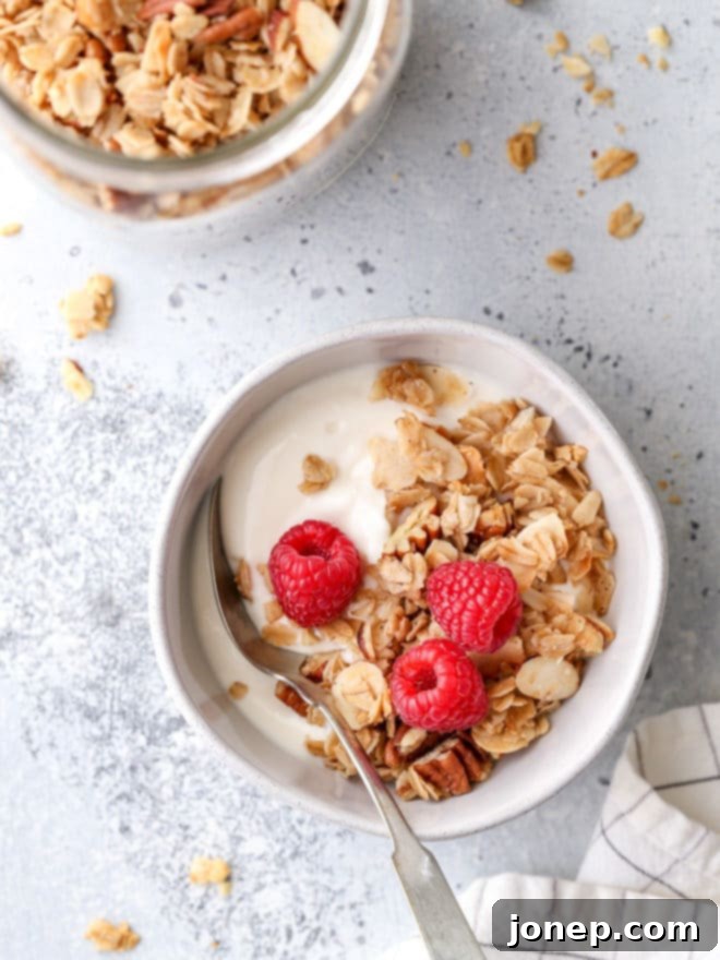 A beautifully styled shot of a glass jar brimming with homemade granola, with a spoon resting against it, highlighting its inviting texture.