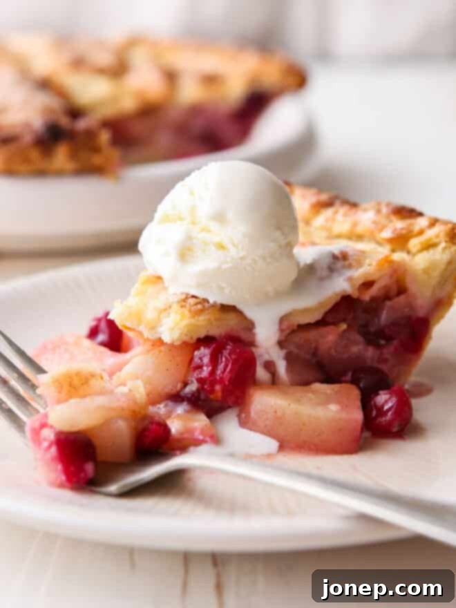 Crimson Pear Delight 6 Closeup of a freshly sliced cranberry pear pie, featuring a golden crust, with a fork and a scoop of vanilla ice cream in the background.