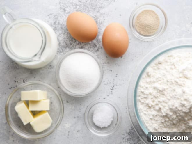 Assorted ingredients for white dinner rolls laid out on a countertop, including flour, yeast, butter, milk, eggs, sugar, and salt.