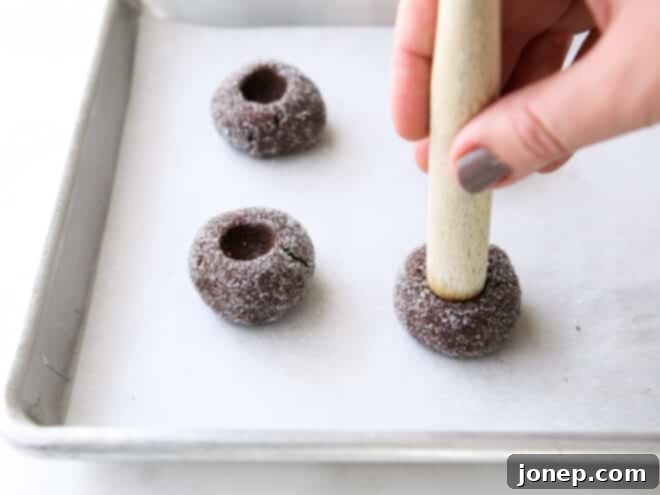 Thumbprints being made in chocolate cookie dough balls with a wooden spoon