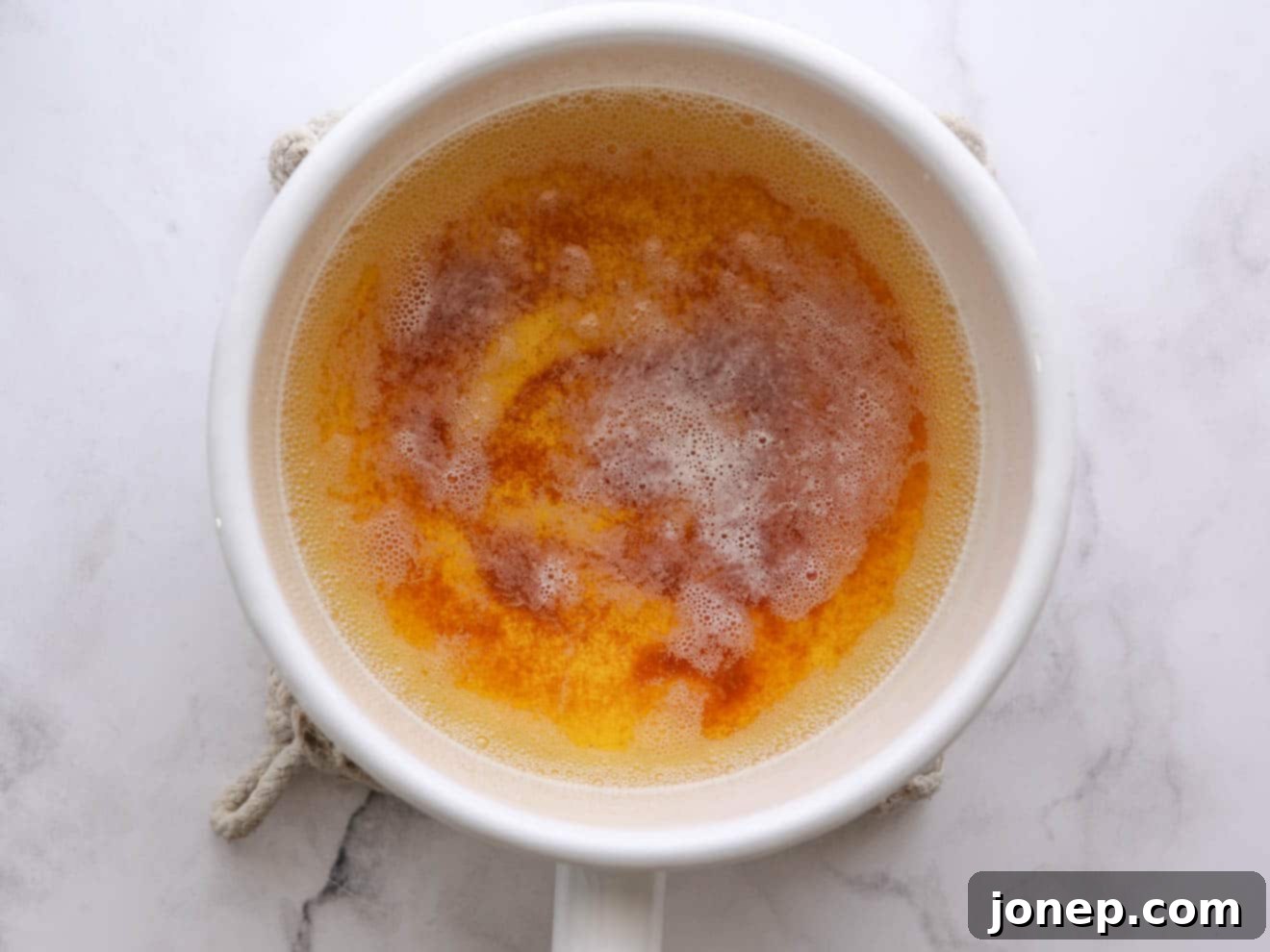 Browned butter cooling in a saucepan, showing its rich amber color and nutty specs, ready to be transferred.