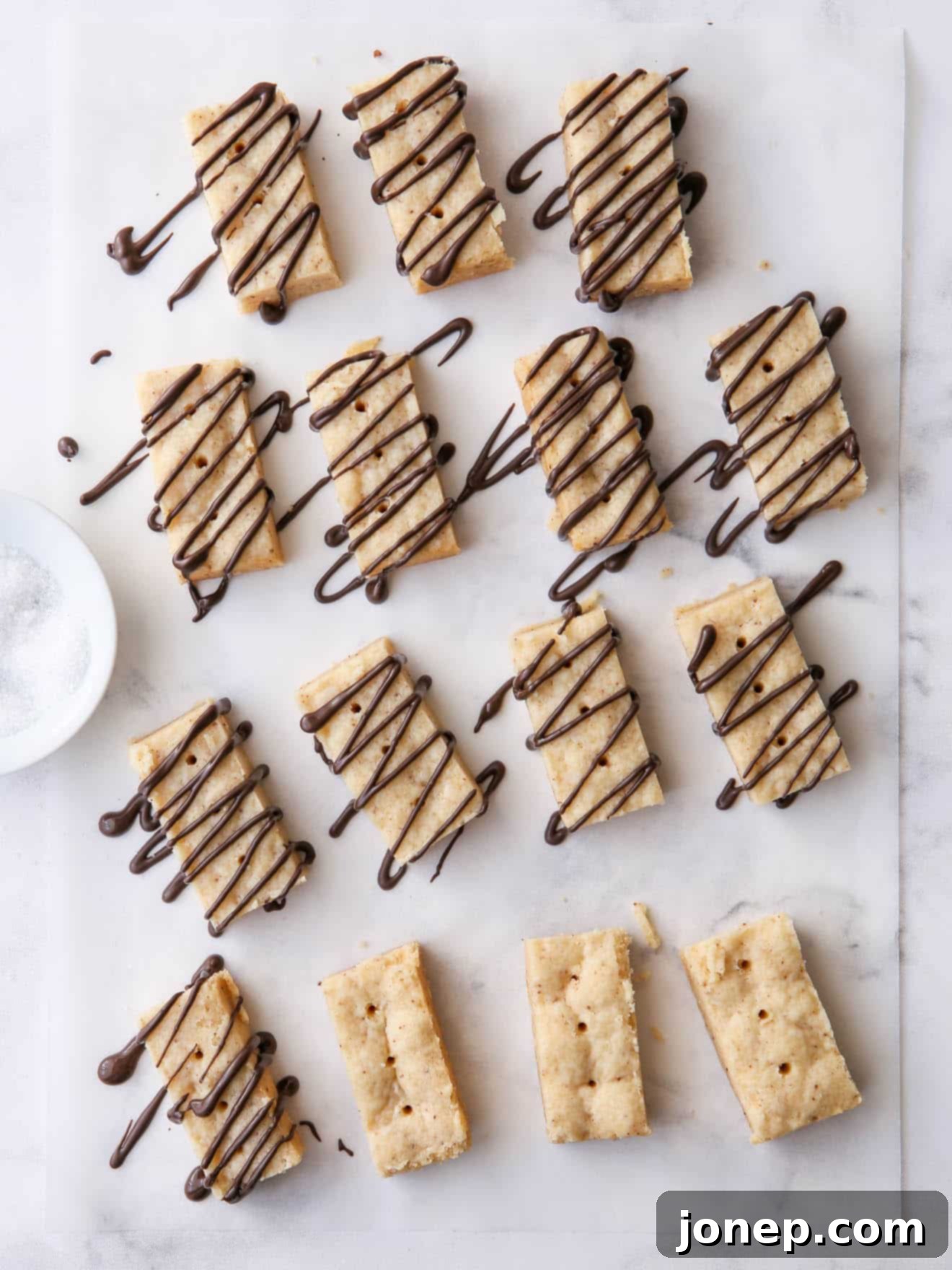 Brown butter shortbread cookies artfully arranged on parchment paper, some adorned with a elegant drizzle of melted chocolate.