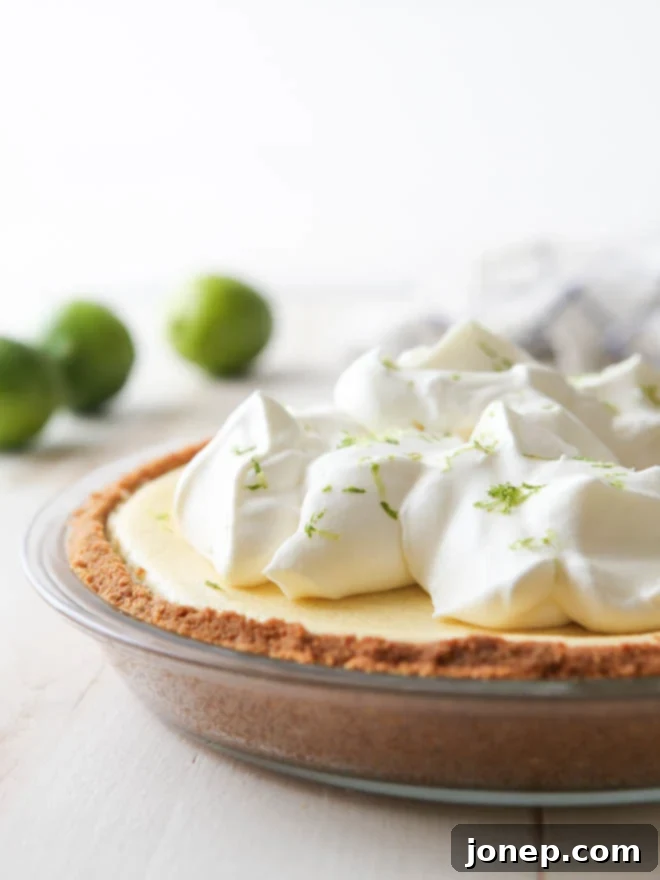 A slice of light and creamy tequila lime pie with a macadamia nut crust, garnished with a lime wedge and whipped cream.