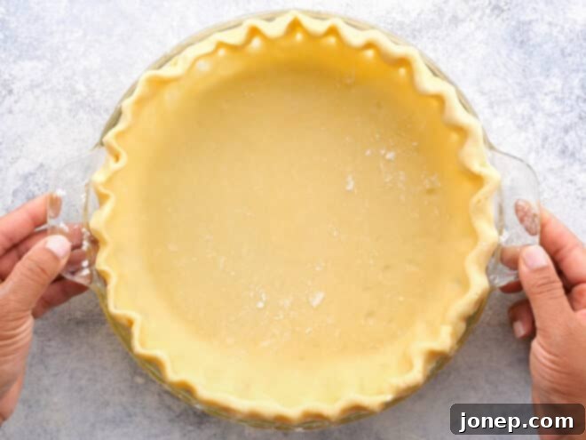 Master Blind Baking for Flawless Pie Crusts 4 Unbaked pie crust carefully fitted into a metal pie dish with decorative crimped edges, ready for chilling.