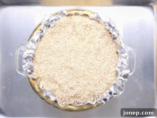 Master Blind Baking for Flawless Pie Crusts 6 Partially baked pie crust still filled with pie weights, showing the foil liner and how the weights reach the top of the crimped edges.