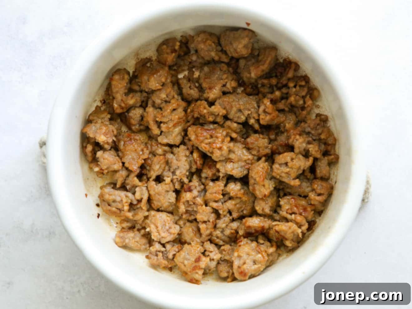 Close-up image of browned Italian sausage crumbles in a pot, showing golden caramelized bits for flavor.