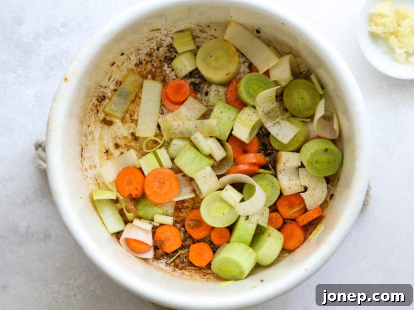 Chopped carrots and leeks sautéing in a pot with olive oil, softening and developing flavor before adding other ingredients.