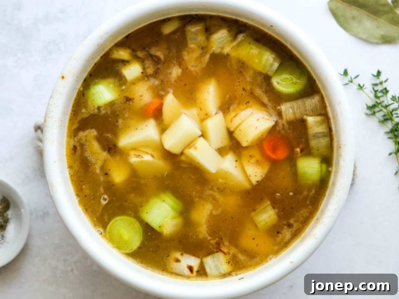 Adding chopped potatoes, broth, and white wine to the sautéed vegetables in a pot, ready for simmering.